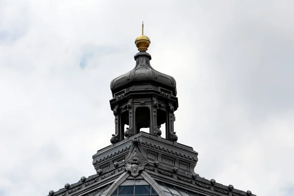 曇り空の背景に様々な装飾的な要素で囲まれたガラスと金属の屋根タイルと古い建物の上に黄金の先端を持つバロック様式のドーム — ストック写真