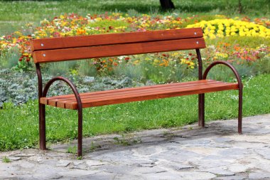 Sıcak güneşli bahar gününde yerel parkta kesilmemiş çim ente ve çiçeklerle çevrili taş karokaldırım üzerinde metal çerçeveli Retro vintage ahşap kamu bank