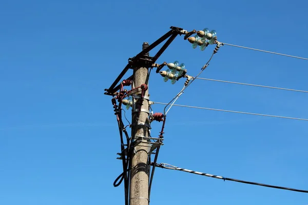 Concrete utility pole with multiple electrical wires connected with ceramic and glass insulators on clear blue sky background