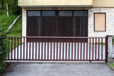 Kapalı metal çit kapıları ve garaj sıcak güneşli yaz gününde kesilmemiş çim ile çevrili doğru giden Döşeli banliyö aile evi driveway