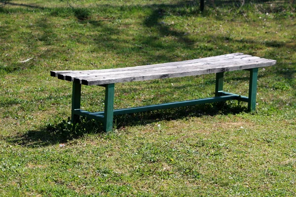 Old public park bench with wooden seat and green metal support frame surrounded with freshly cut grass in local park on warm sunny spring day