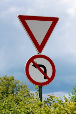 Yol ver ve hiçbir sol ayarı kırmızı ve beyaz işaretler bulutlu fırtınalı mavi gökyüzü arka plan üzerinde yoğun yaprakları ile çevrili güçlü metal kutup üzerine monte