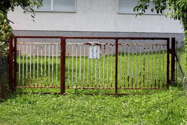 Kapalı kapılar ve sıcak güneşli yaz gününde kesilmemiş çim ve diğer bitkiler ile çevrili monte posta kutusu ile tamamen paslı beyaz eski metal çit
