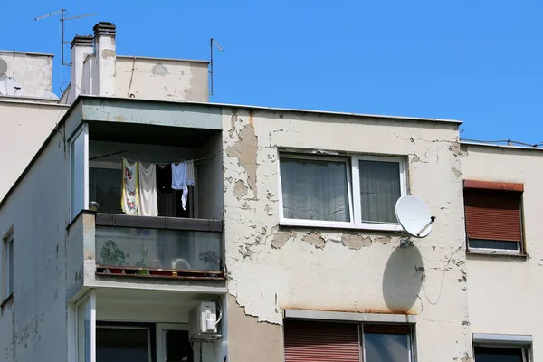 Single apartment with windows and open balcony surrounded with dilapidated cracked old facade and other apartments on clear blue sky background