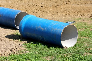 Açık mavi büyük çaplı inşaat boruları inşaat sahasında bırakıldı. Sıcak yaz gününde çimenler ve kuru toprakla çevrili.