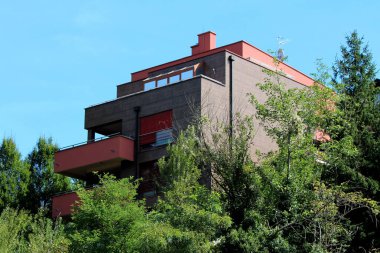 Sıcak yaz gününde, yoğun orman ve açık mavi gökyüzü ile çevrili geniş balkonlu, yeni inşa edilmiş çok katlı bir banliyö evi.