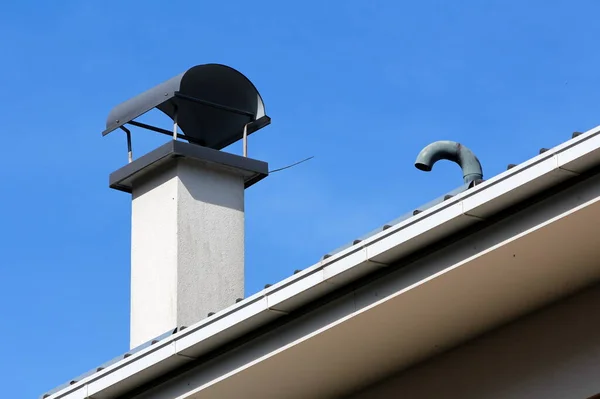 新烟囱 在现代家庭房顶上有深色金属保护顶 周围是灰色的排水沟和蓝天背景的弯曲烟斗 — 图库照片