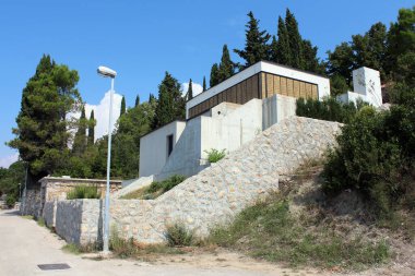 Tasarım gibi bir sığınağı ve kapalı pencere perdeleri olan bitmemiş garip görünümlü bir aile evi. Sıcak yaz gününde, geleneksel taş duvarlar ve sık ağaçlarla çevrili.