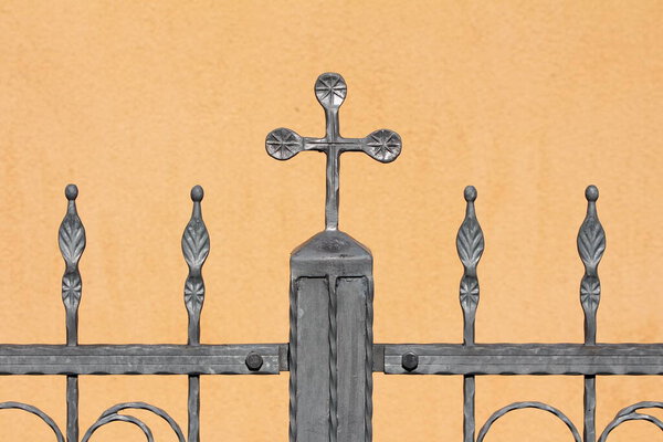 Винтажный ретро серый кованый железный забор с многочисленными пользовательскими украшения в форме маленьких цветов, чтобы большой крест на верхней части сильной опоры столб на светло-коричневом фасаде пригородного семейного дома