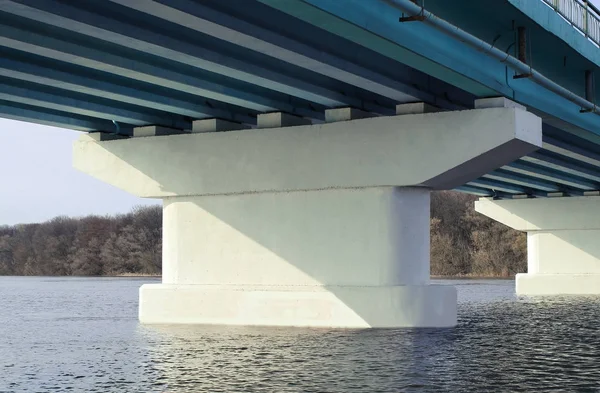 Piles under the bridge. Long concrete bridge across a wide river on a Sunny day. Bottom view