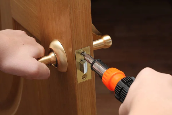 man with a screwdriver in his hand repairs the inner door. door lock. hands close up