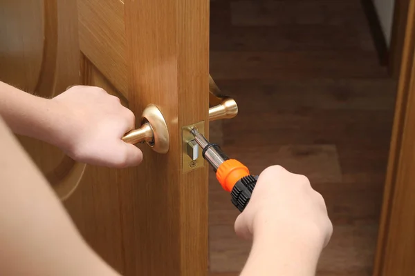 man with a screwdriver in his hand repairs the inner door. door lock. hands close up