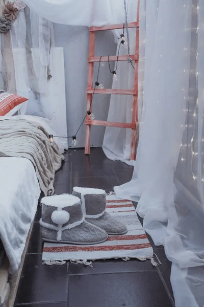 Stylová ložnice v šedých tónů, teplé boty na Mat poblíž postele z palet. — Stock fotografie