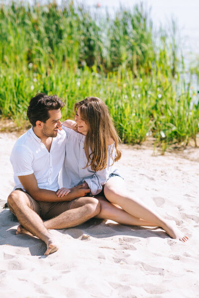 happy couple sitting on sandy city beach and looking at each other