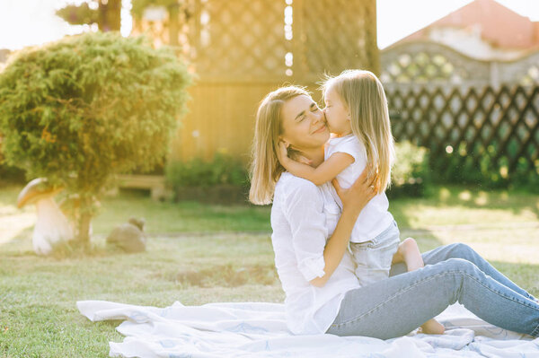 happy mother and little daughter hugging each other while resting on cloth together on backyard