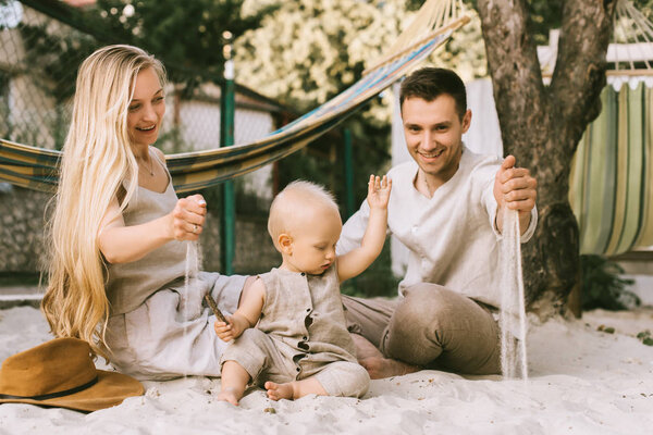 улыбающиеся родители и маленький сын играют с песком на земле вместе в сельской местности
