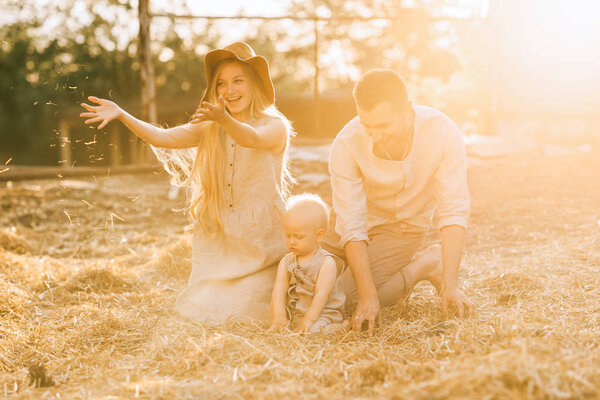 happy parents and little son in linen clothing resting on hay at countryside