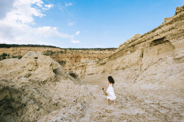 back view of girl in white dress walking in sand canyon with blue sky 
