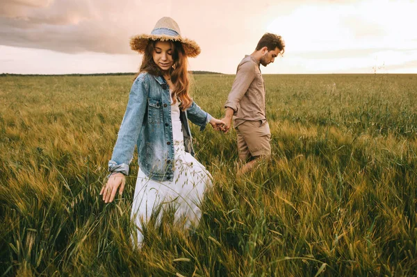 スタイリッシュなカップル手を繋いでいると 緑の草原の上を歩く — ストック写真