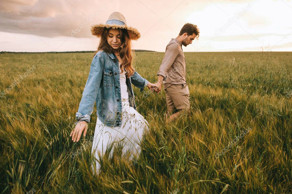 stylish couple holding hands and walking on green meadow