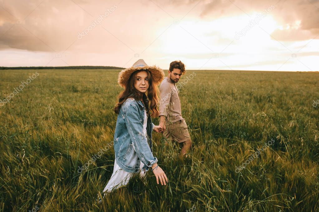 attractive stylish couple holding hands and walking on green meadow