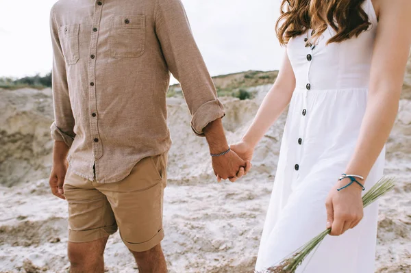 スタイリッシュなカップルは手を繋いでいると砂の渓谷を歩いてのビューをトリミング — ストック写真