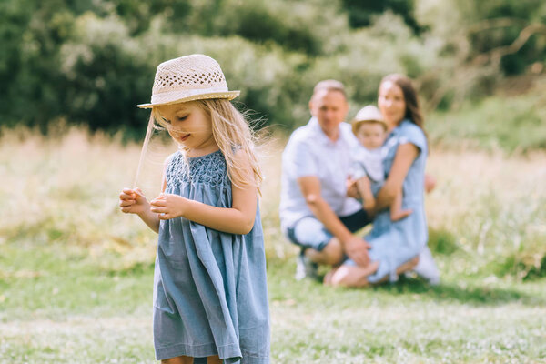маленькая девочка в соломенной шляпе летом feild с семьей позади

