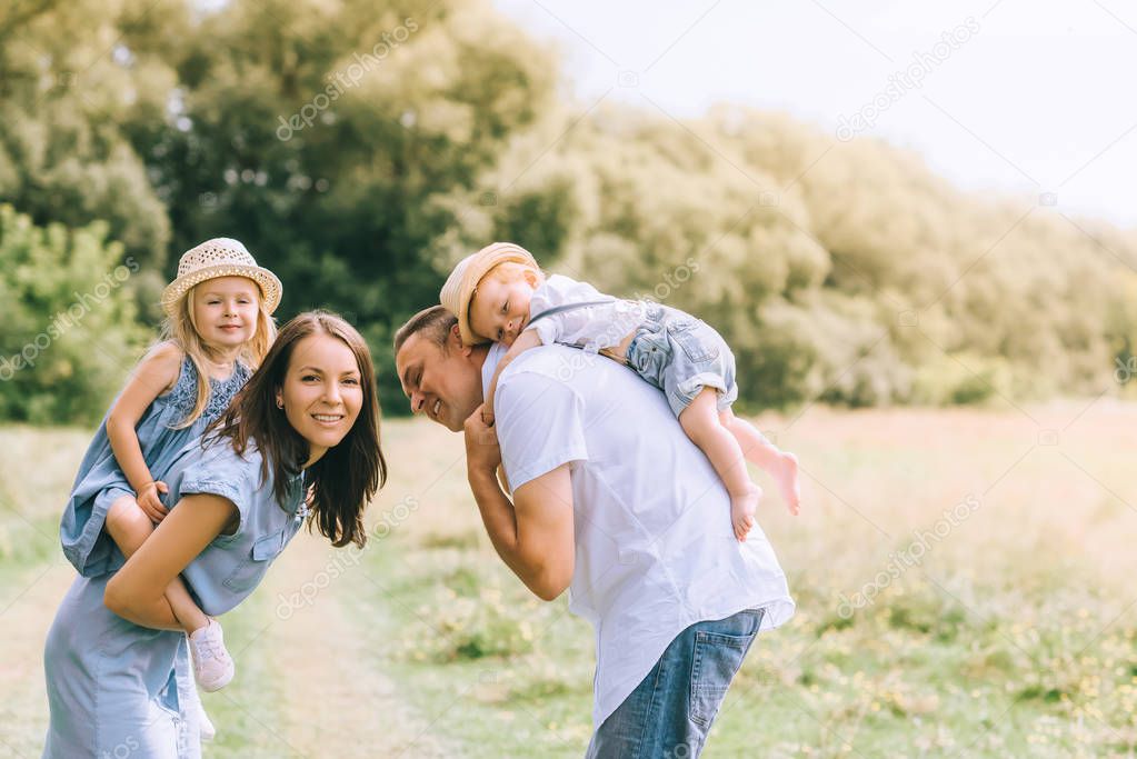 happy parents piggybacking son and daughter in straw hats on summer feild