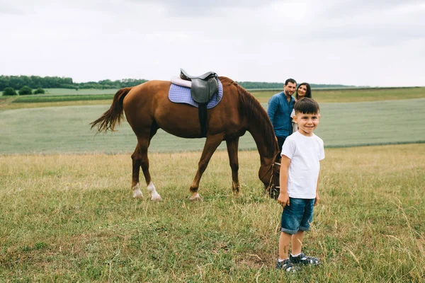 parents standing near horse, smiling son looking at camera on field