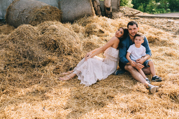 happy parents and son sitting on hay and looking at camera