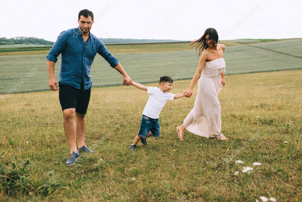 parents and son holding hands on field 