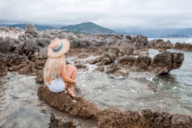 kız bikini üst ve Karadağ'daki kayalık plajda otururken hasır şapka