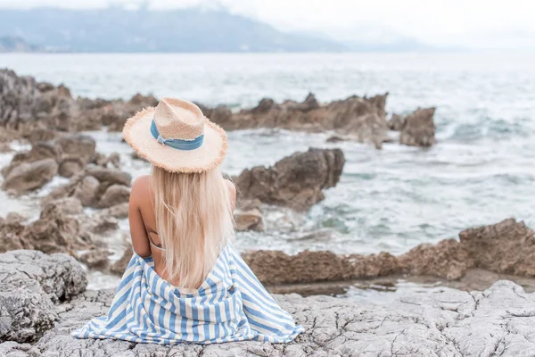 モンテネグロの岩のビーチに座っている麦わら帽子の女の子の背面図 — ストック写真