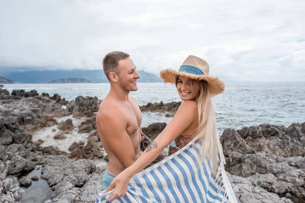 美丽快乐的年轻夫妇站在一起在黑山岩石海滩的侧面视图 — 图库照片