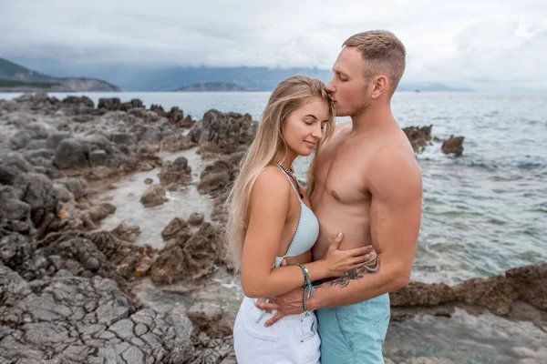 美丽温柔的年轻情侣的侧面视图在黑山的岩石海滩拥抱和亲吻 — 图库照片