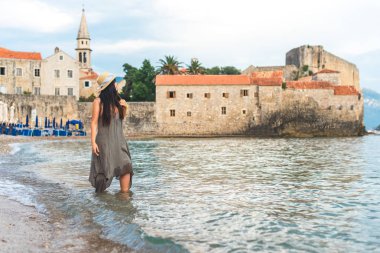 woman standing in Adriatic sea with Bell Tower of Sveti Ivana Cathedral on background in Budva, Montenegro clipart