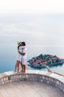 couple hugging on viewpoint near island of Sveti Stefan with hotel resort in Adriatic sea, Budva, Montenegro clipart