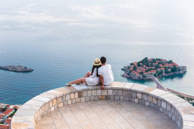 couple hugging on viewpoint and looking at island of Sveti Stefan in Budva, Montenegro  clipart