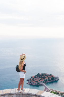 woman standing on viewpoint and looking at saint stephen island in Adriatic sea, Budva, Montenegro  clipart