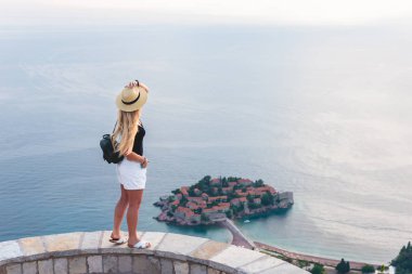 woman standing and looking at saint stephen island in Adriatic sea, Budva, Montenegro  clipart