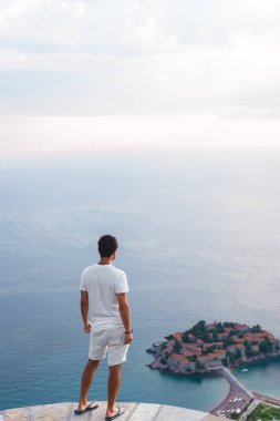 back view of man looking at island of Sveti Stefan with hotel resort in Adriatic sea, Budva, Montenegro clipart