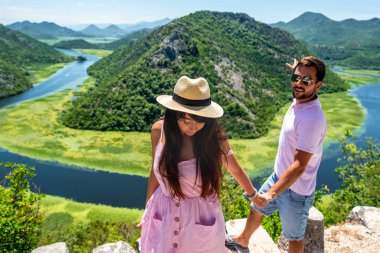 couple in pink clothes holding hands near Crnojevica River (Rijeka Crnojevica) in Montenegro clipart