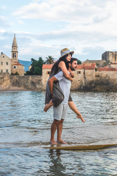 boyfriend giving piggyback to girlfriend on Ricardova Glava beach in Budva, Montenegro