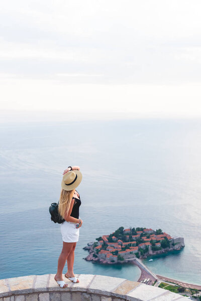 woman standing on viewpoint and looking at saint stephen island in Adriatic sea, Budva, Montenegro 