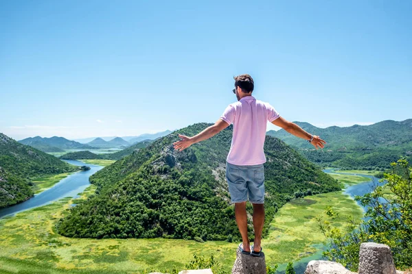 モンテネグロの Crnojevica 川に近い視点の石に立っているピンクのシャツの男の背面します  — 無料ストックフォト