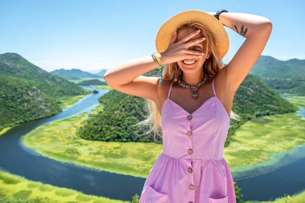穿粉红色礼服和帽子的妇女看着相机通过手指在黑山 Crnojevica 河附近 — 图库照片