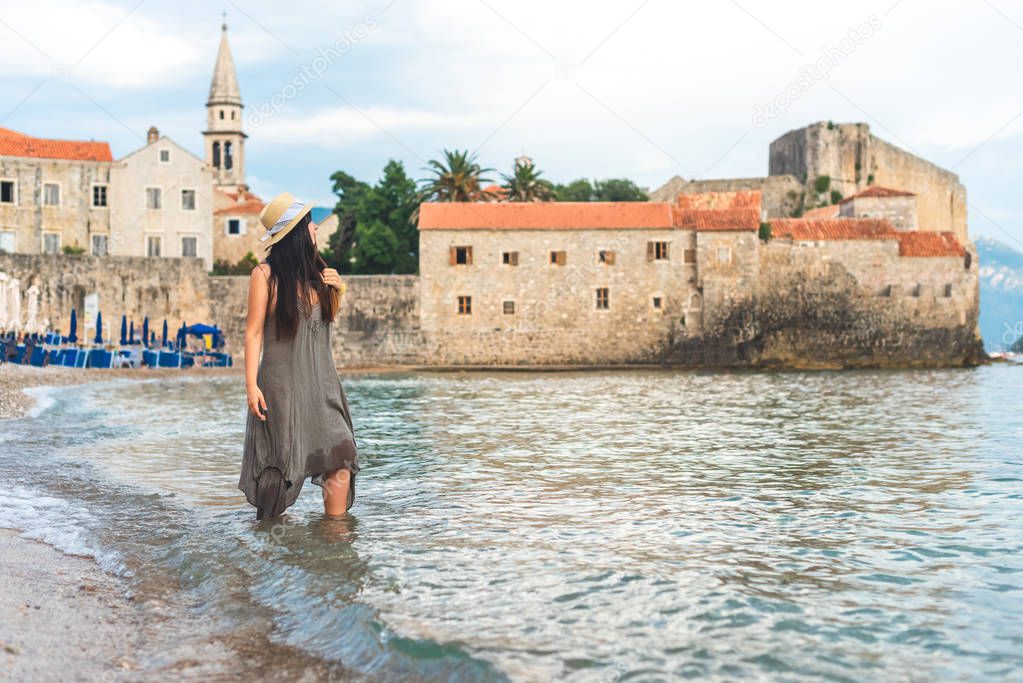 woman standing in Adriatic sea with Bell Tower of Sveti Ivana Cathedral on background in Budva, Montenegro