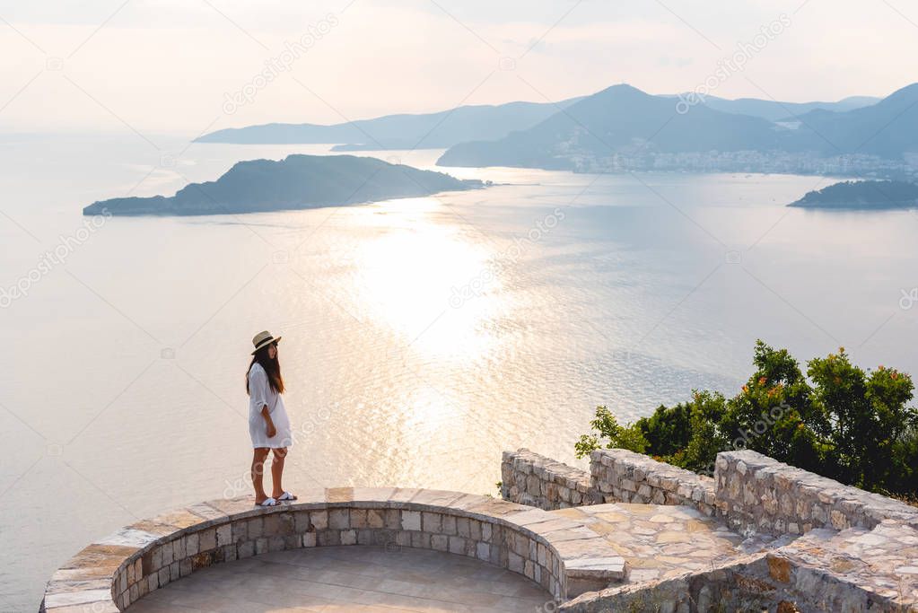 woman standing on viewpoint near Adriatic sea during sunset in Budva, Montenegro