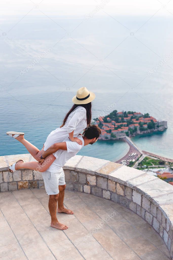 boyfriend giving piggyback to girlfriend at viewpoint near island of Sveti Stefan in Budva, Montenegro