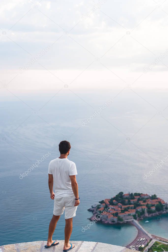 back view of man looking at island of Sveti Stefan with hotel resort in Adriatic sea, Budva, Montenegro